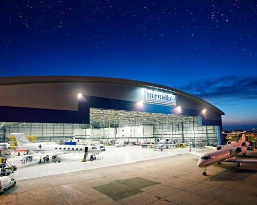 Exterior of Gulfstream International Service Facility at night with planes within the hangar.